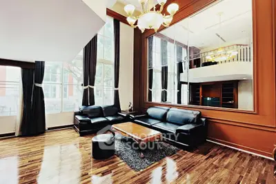 Luxurious double-height living room with elegant black leather sofas and large windows.