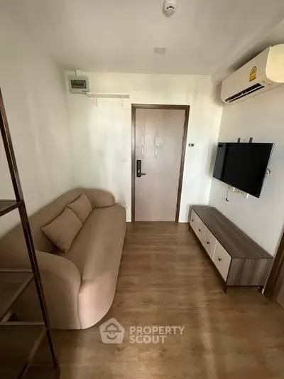 Cozy living room with modern sofa, wall-mounted TV, and wooden flooring in a compact apartment.