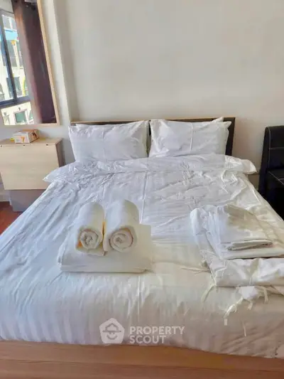 Cozy bedroom with neatly arranged white linens and natural light from a window, perfect for relaxation.