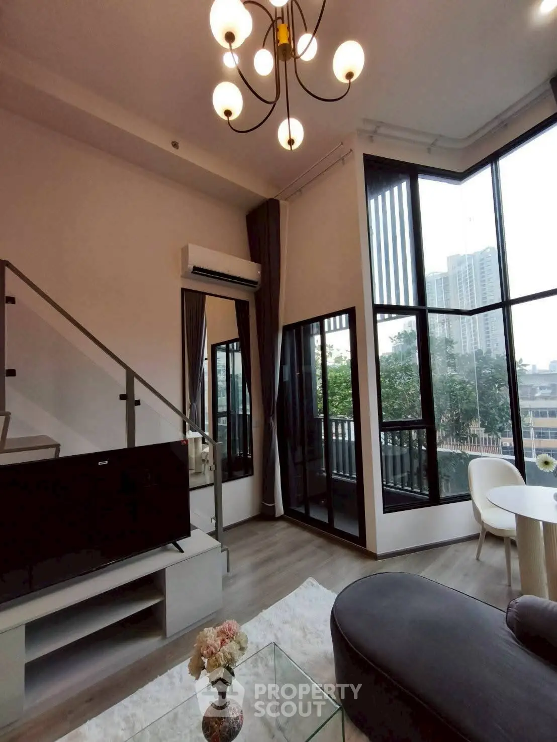 Modern living room with high ceilings, large windows, and stylish chandelier in urban apartment.
