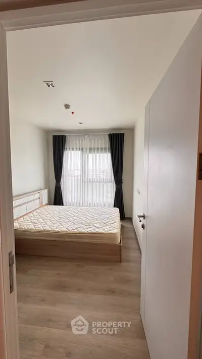 Spacious bedroom with large window and elegant curtains, featuring a comfortable bed and wooden flooring.