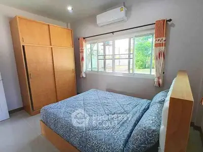 Cozy bedroom with large window and wooden wardrobe, perfect for relaxation.