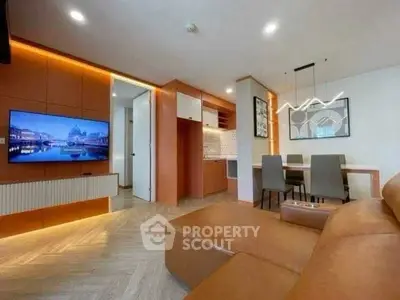 Modern living room with stylish decor and open kitchen layout, featuring a large TV and elegant lighting.