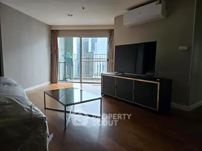 Modern living room with large TV and balcony view in high-rise apartment.