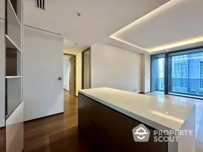 Modern open-plan kitchen with sleek island and large windows in luxury apartment.