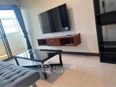 Modern living room with wall-mounted TV and glass coffee table in a bright apartment.