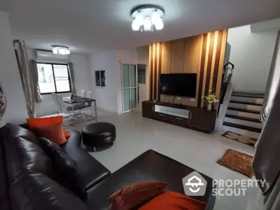 Modern living room with leather sofa and TV, open dining area, and staircase.