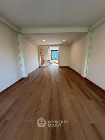 Spacious empty room with wooden flooring and bright natural light, ideal for customization.