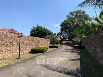 Charming stone-walled driveway leading to a serene residential property with lush greenery.