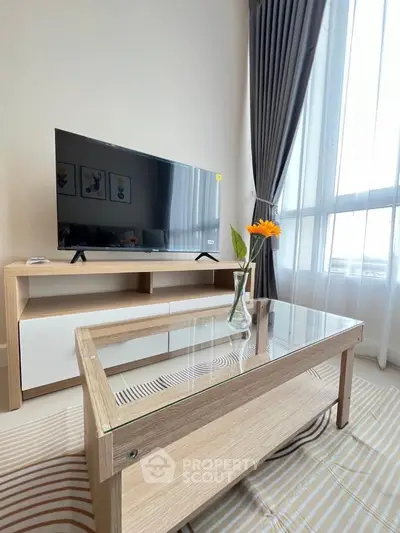 Modern living room with stylish TV stand and glass coffee table, featuring large windows and elegant curtains.