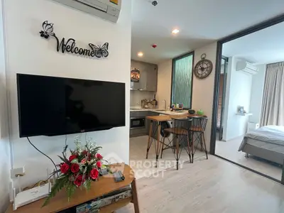 Modern open-layout living room with kitchen and bedroom view, featuring stylish decor and wall-mounted TV.