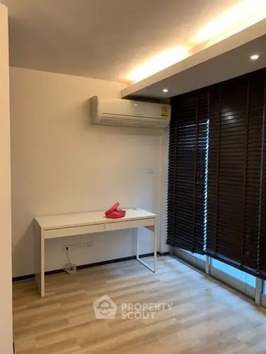 Modern minimalist bedroom with sleek white desk, ambient lighting, and large window with dark blinds, perfect for serene living.