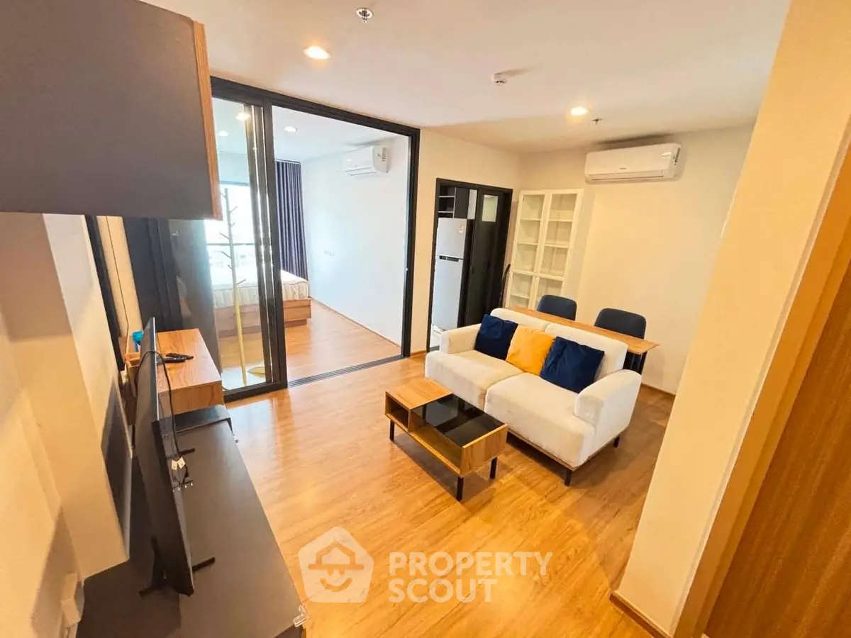 Modern living room with wooden flooring, cozy sofa, and glass partition leading to bedroom.