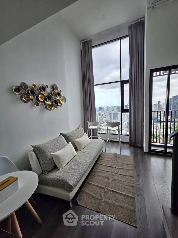 Modern living room with high ceilings and city view, featuring stylish decor and floor-to-ceiling windows.