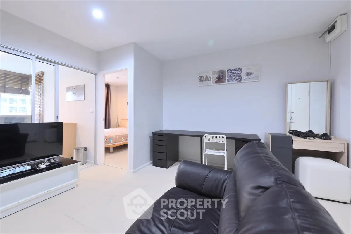 Modern living room with sleek leather sofa and open view to bedroom, featuring stylish decor and ample natural light.