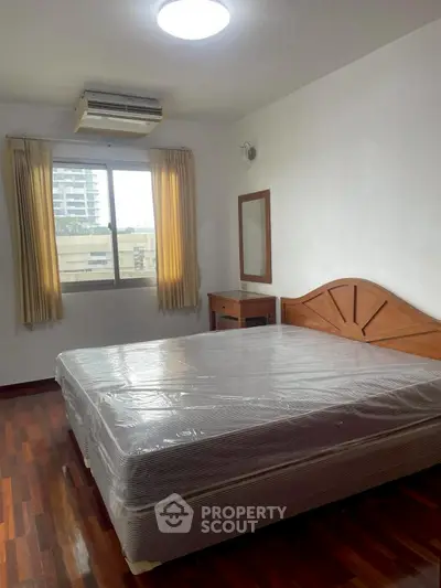 Spacious bedroom with large window and wooden flooring, featuring a comfortable bed and air conditioning.