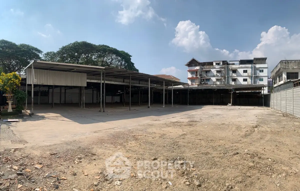 Spacious open lot with potential for development, featuring adjacent buildings and clear sky view.