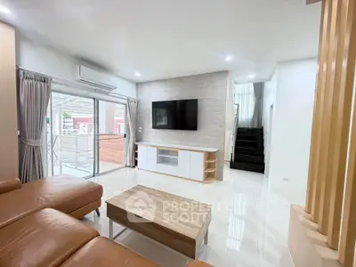 Spacious modern living room with leather sofa and wall-mounted TV, featuring natural light and stylish decor.