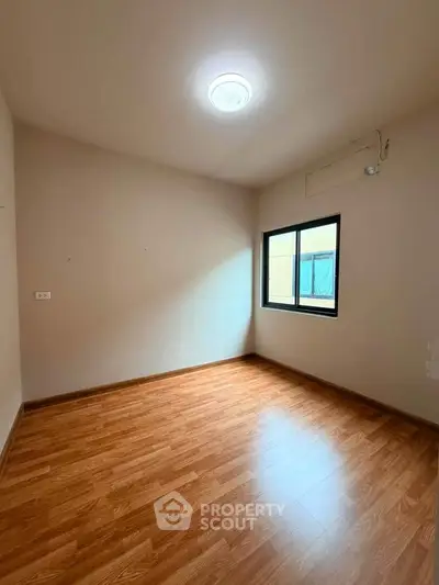 Spacious empty room with wooden flooring and natural light from window