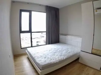 Modern bedroom with large window and wooden flooring in a stylish apartment.