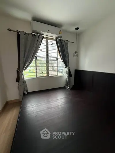 Spacious bedroom with dark wood flooring and large window for natural light.