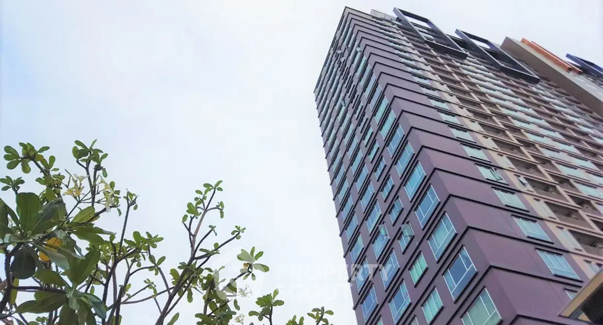 Modern high-rise building with lush greenery and clear sky view.