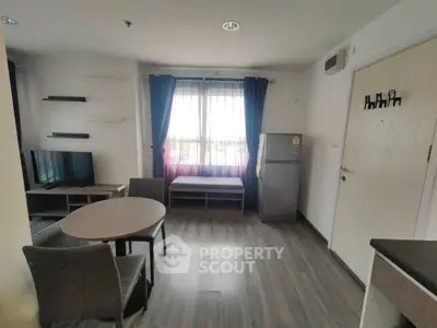 Modern living room with dining area and natural light, featuring a TV and refrigerator.