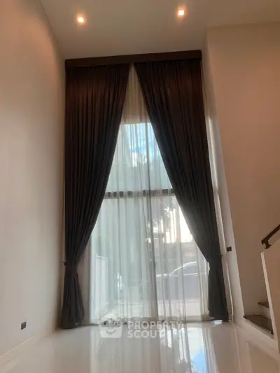 Elegant high-ceiling room with floor-to-ceiling windows and luxurious curtains, perfect for modern living.