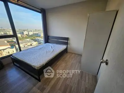 Bright bedroom with large window offering city view and wooden flooring.