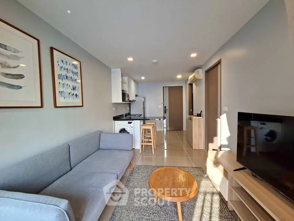 Modern living room with open kitchen, featuring sleek furniture and bright natural lighting.