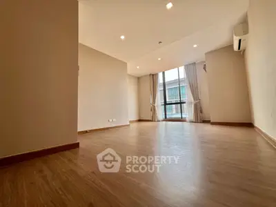 Spacious empty living room with wooden flooring and large window.