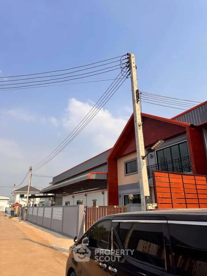 Modern industrial-style building with red accents and spacious parking area under clear blue sky.