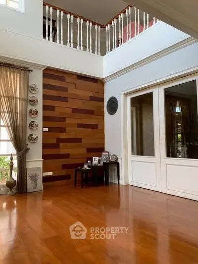 Elegant living room with wooden flooring and high ceiling, featuring decorative wall panels and natural light.
