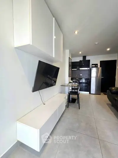 Modern living room with sleek white cabinets and wall-mounted TV, open to a stylish kitchen with stainless steel appliances.