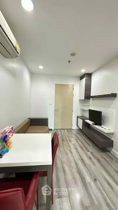 Modern living room with sleek furniture and wooden flooring, featuring a compact dining area and wall-mounted TV.