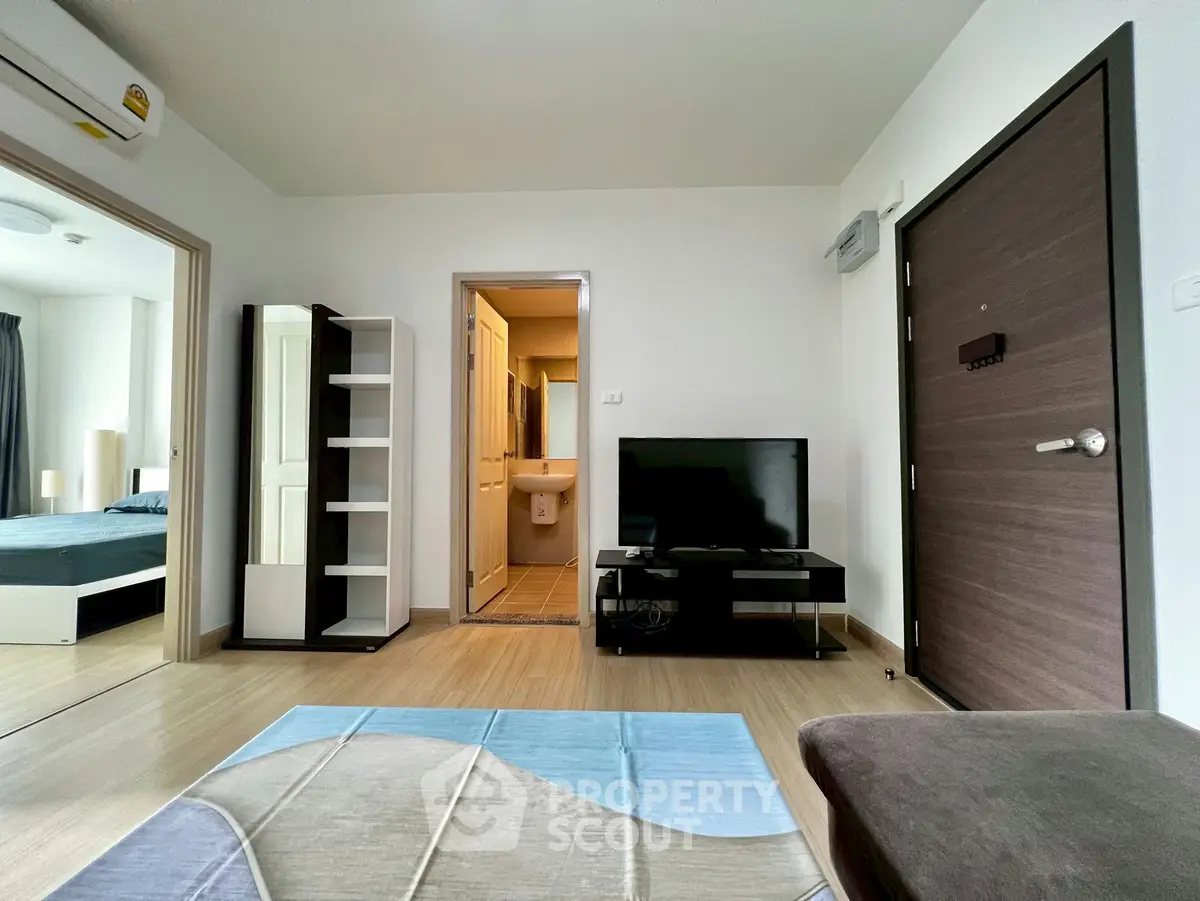 Modern living room with TV, open layout, and view into bedroom and bathroom.