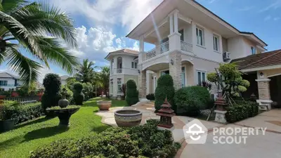 Luxurious two-story villa with manicured garden and elegant architecture under clear blue sky.