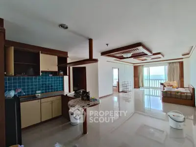 Spacious open-layout living room with kitchen and ocean view, featuring elegant ceiling design and large windows.