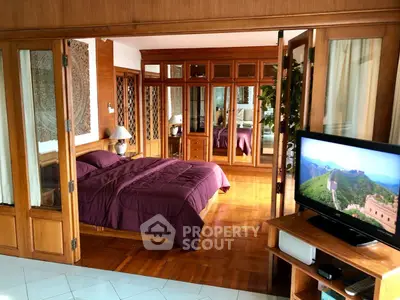 Spacious bedroom with wooden accents and mirrored wardrobe, featuring a cozy bed and a TV for ultimate relaxation.