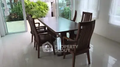 Elegant dining area with wooden table and chairs, overlooking lush garden through glass doors.