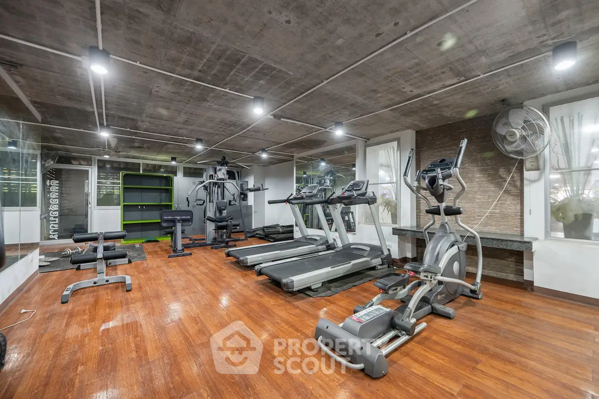 Spacious modern gym with state-of-the-art equipment and wooden flooring in a luxury residential complex.