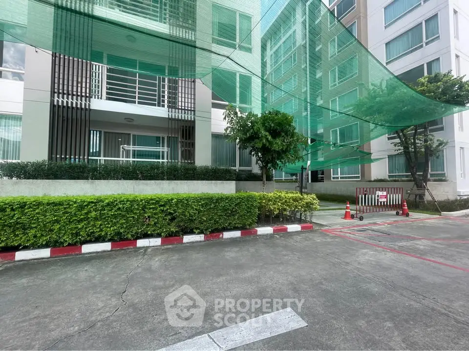 Modern apartment building exterior with green landscaping and parking area.