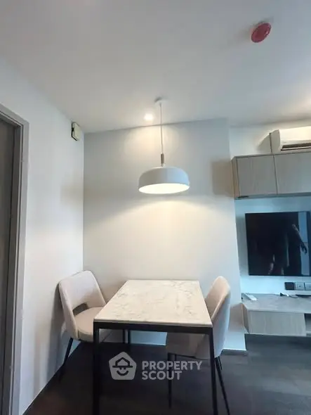 Modern dining area with sleek table and chairs, stylish lighting, and wall-mounted TV in a contemporary apartment.