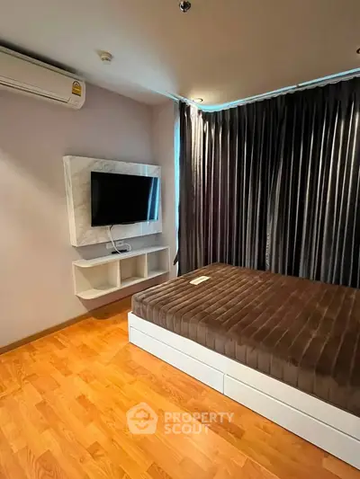 Modern bedroom with wooden flooring, wall-mounted TV, and elegant curtains.