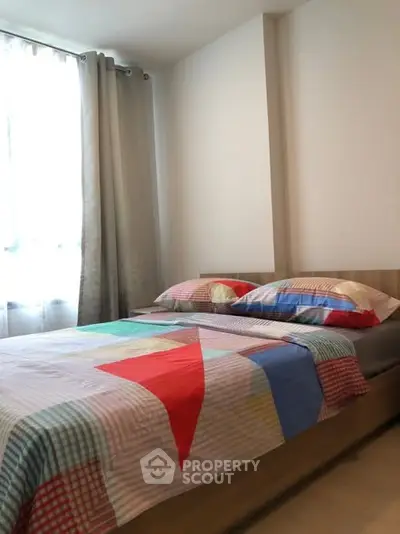 Cozy bedroom with colorful bedding and natural light from large window.