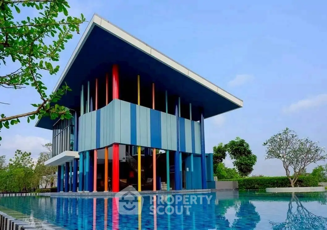 Modern architectural building with vibrant colors and poolside view, surrounded by lush greenery.