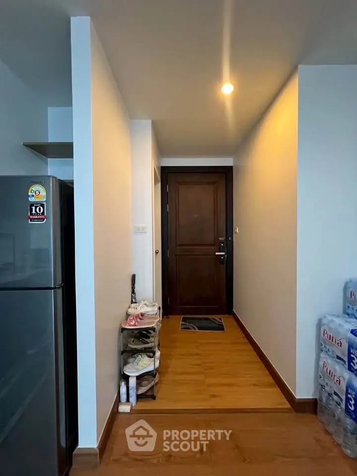 Modern apartment entrance with wooden flooring and shoe rack, adjacent to a sleek refrigerator.
