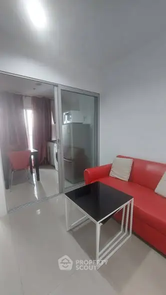 Modern living room with red sofa and glass partition leading to dining area.