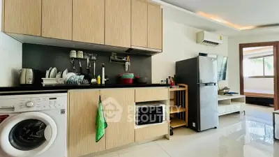 Modern kitchen with washing machine, fridge, and microwave in open layout apartment.