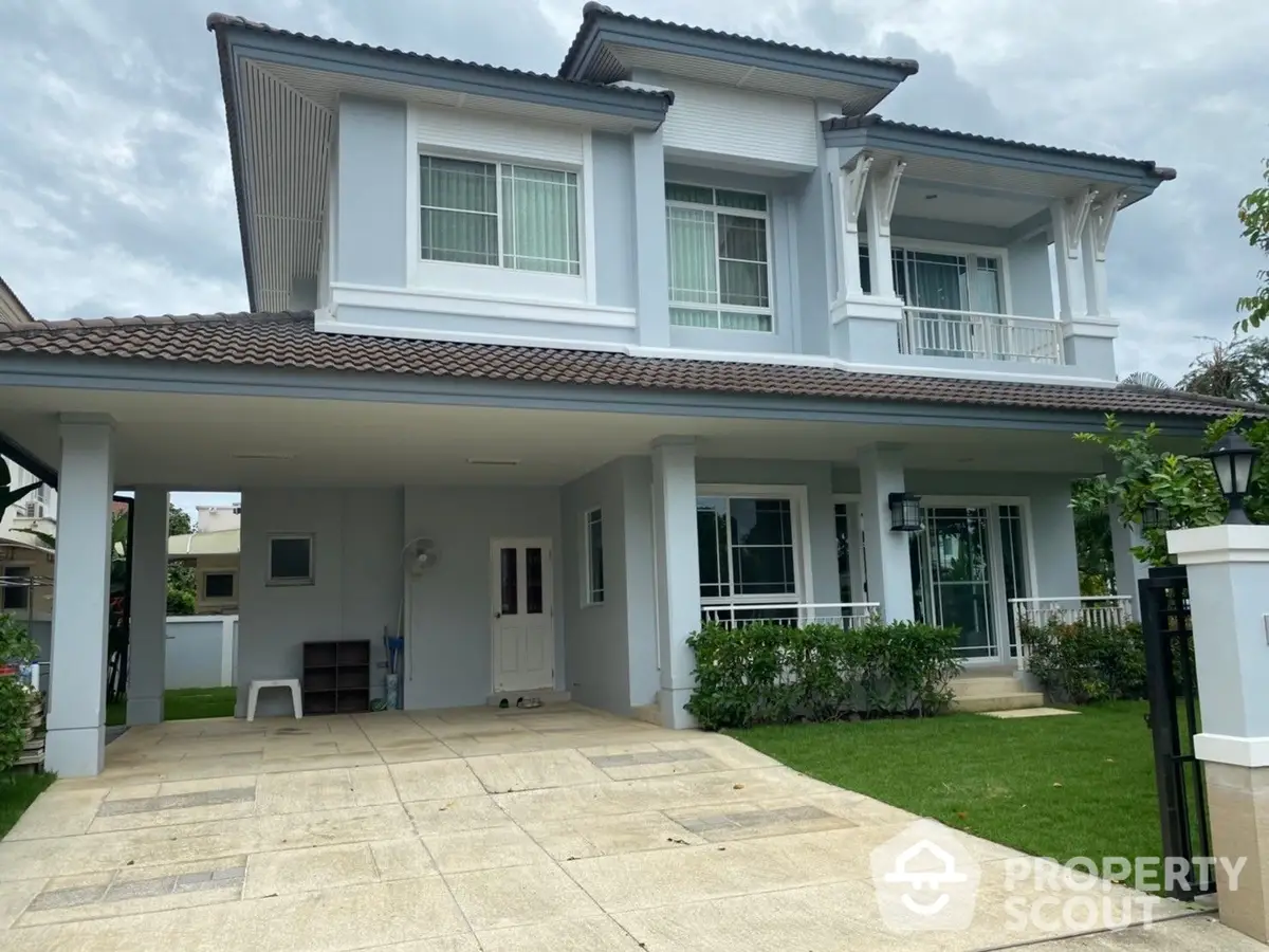 Elegant two-story house with a spacious covered carport and a lush green lawn, featuring a large balcony and classic white exterior.